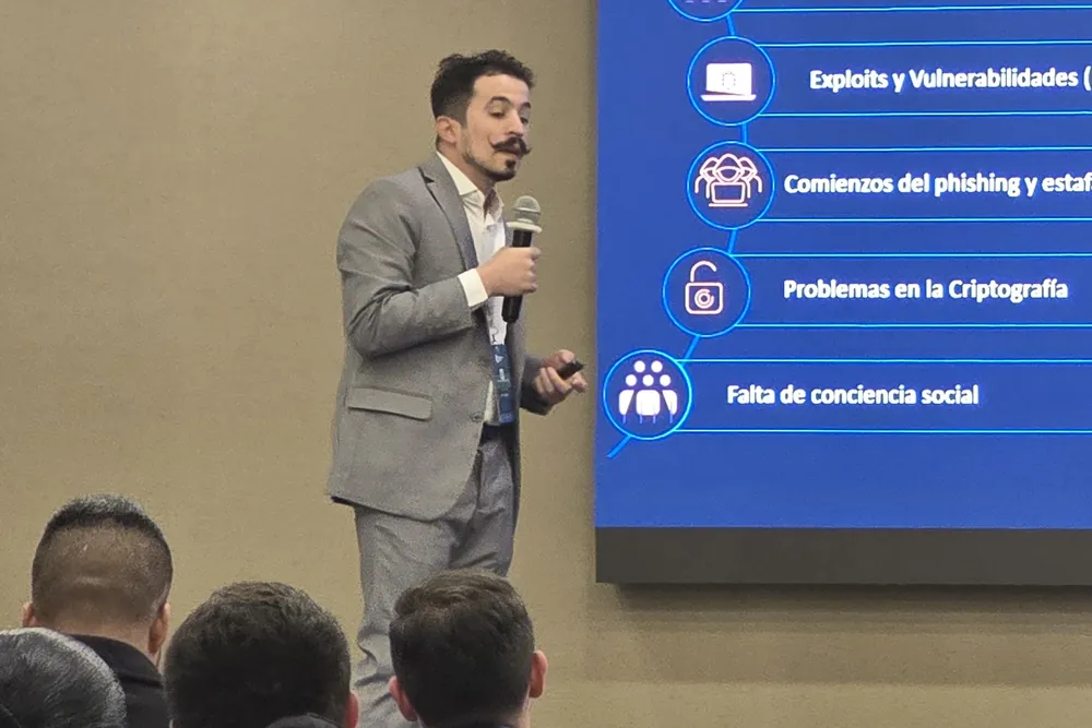 Especialista de ColCiber, con micrófono, dictando ante un auditorio una charla sobre amenazas de ciberseguridad; en la pantalla se leen las categorías que va explicando.